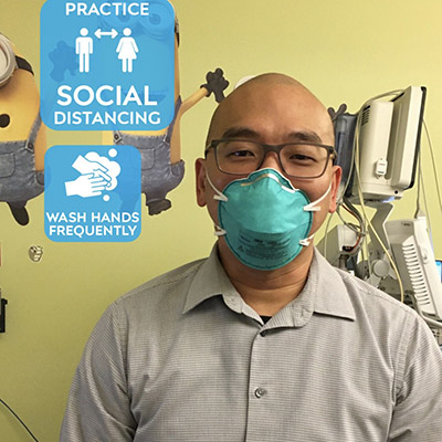 A healthcare worker in a mask beside a social-distancing and hand-washing reminder