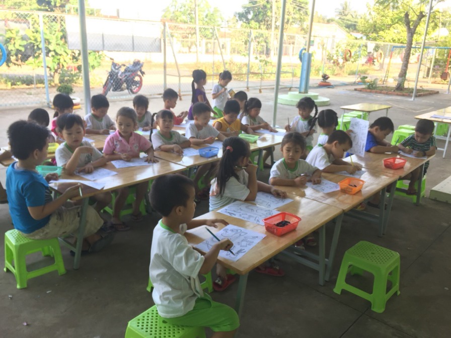 Young children drawing at long tables in a village classroom in Vietnam